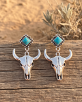 Silver turquoise bull skull drop earrings on rustic wood