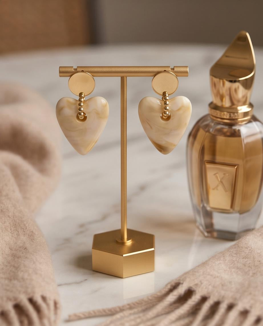 Cream marble heart drop earrings on gold display stand with perfume bottle