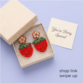Red strawberry beaded drop earrings on pink background