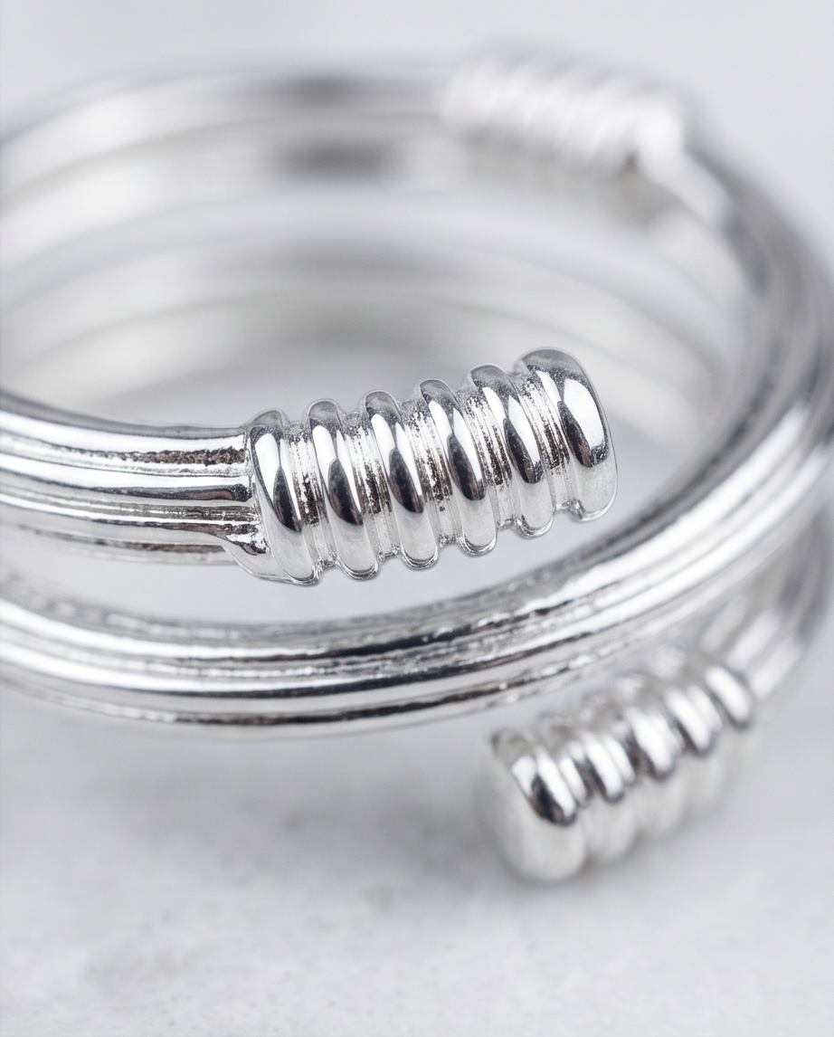 Model wearing silver coil wrap ribbed end open ring on index finger against grey silk