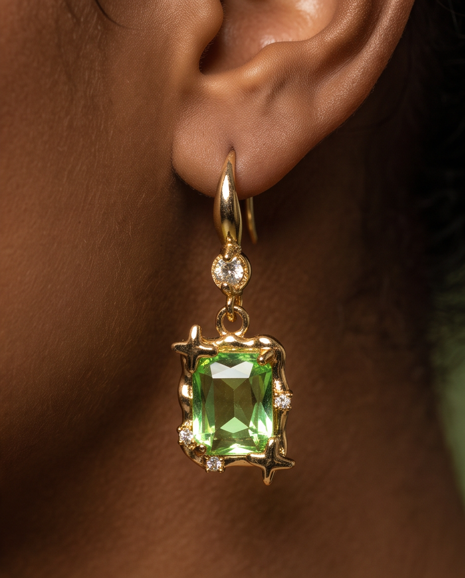Pair of gold tone peridot green emerald-cut crystal star frame hook drop earrings on dewy lily pad with moss