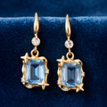 Model in fairytale ball gown wearing gold tone aquamarine crystal star frame drop earrings with Cinderella carriage backdrop