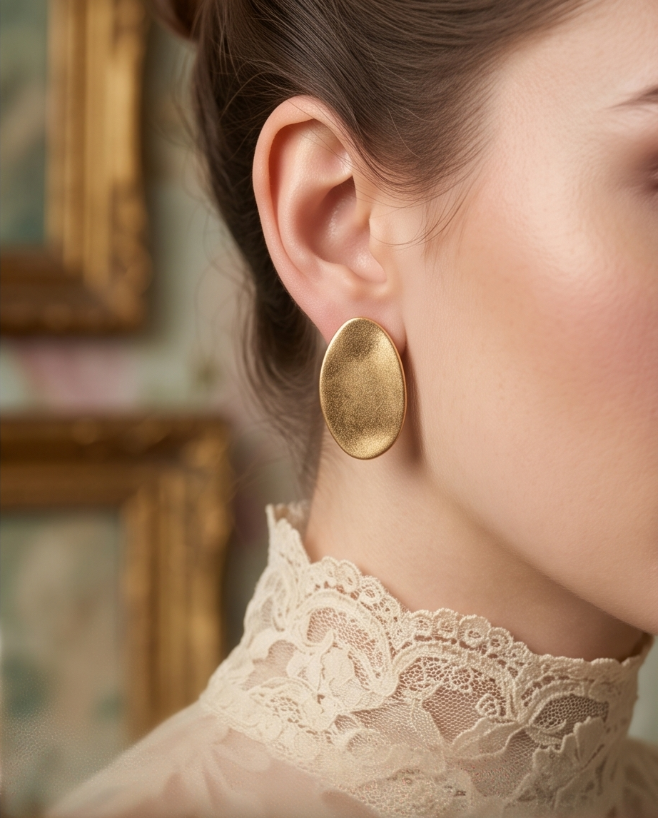 Macro close up of pair of gold tone brushed oval disc stud earrings standing upright on teal velvet showing brushed satin texture