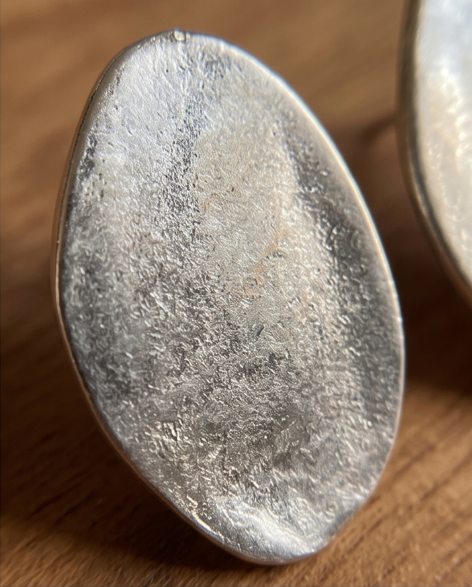 Pair of silver tone brushed oval disc stud earrings on walnut wood tray with linen cloth