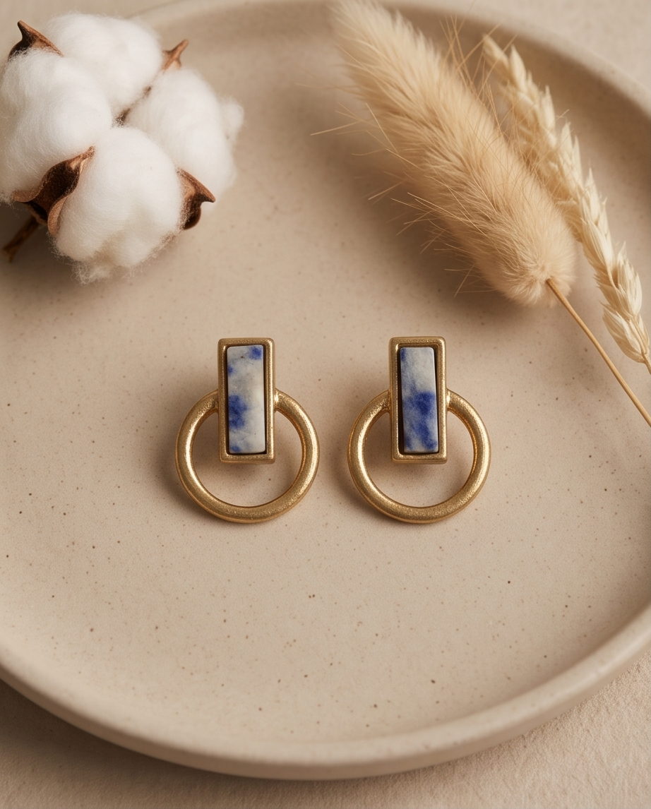 Macro close up of gold tone matte sodalite blue marble rectangle bezel open circle hoop drop earring on sandy surface showing natural stone veining and brushed gold detail