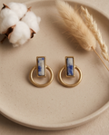 Macro close up of gold tone matte sodalite blue marble rectangle bezel open circle hoop drop earring on sandy surface showing natural stone veining and brushed gold detail
