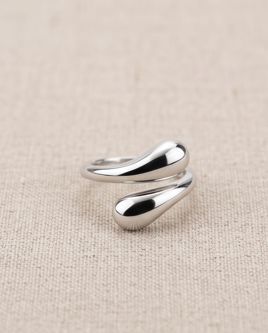Model's hand resting on wooden chair arm wearing 925 silver plated sculptural double teardrop wrap open adjustable ring with cream satin sleeve
