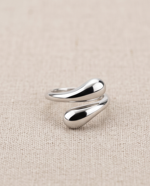 Model's hand resting on wooden chair arm wearing 925 silver plated sculptural double teardrop wrap open adjustable ring with cream satin sleeve