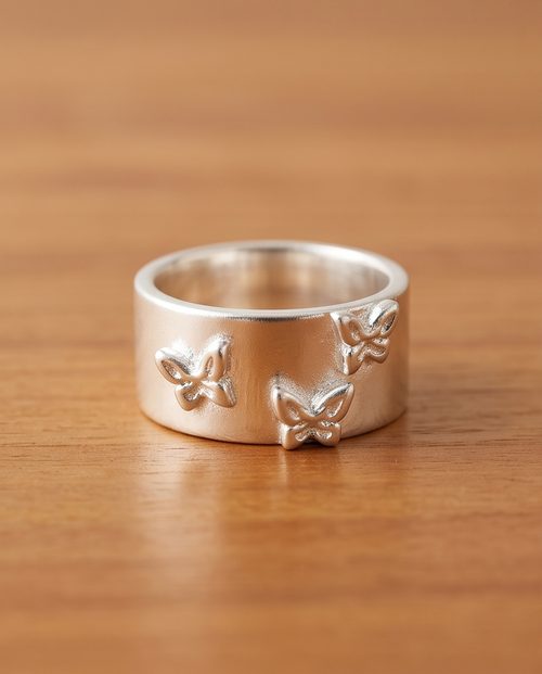 Model's hand resting on rustic wood wearing 925 silver plated matte wide band triple butterfly embossed adjustable ring in warm golden sunlight