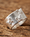 Macro close up of 925 silver plated matte wide band triple butterfly embossed adjustable ring on rustic wood showing raised butterfly motifs and brushed matte texture