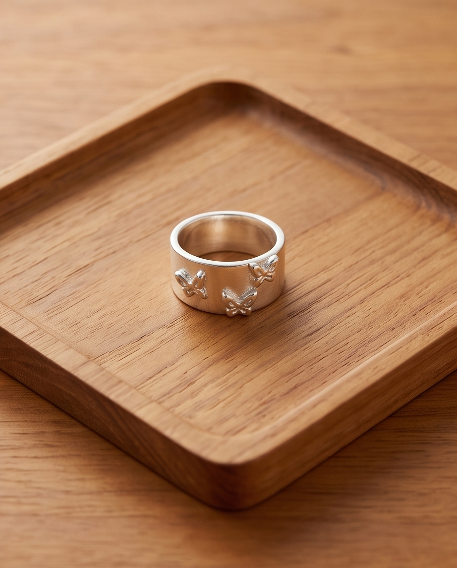 925 silver plated matte wide band triple butterfly embossed adjustable ring on warm wood surface showing three raised butterfly motifs across the band