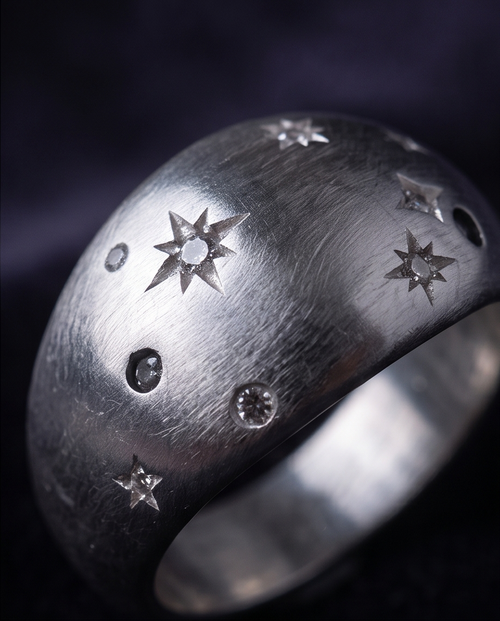 Macro close up of 925 silver plated brushed dome constellation star engraved wide band ring on dark background showing engraved eight-pointed stars and round crystal details across brushed dome surface