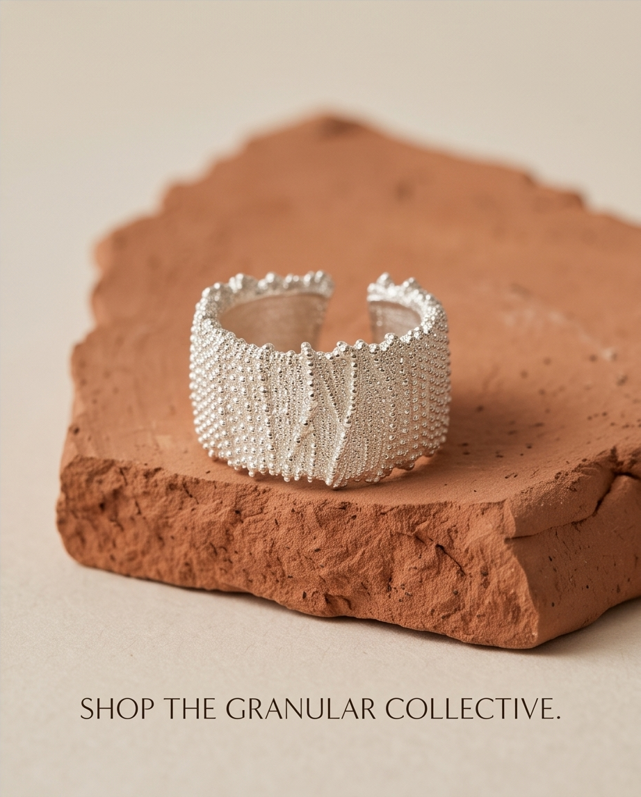 Shop the Granular Collective campaign — 925 silver plated granular textured wide cuff open adjustable ring on terracotta stone plinth on cream background showing full band texture from above