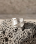 925 silver plated brushed dome sculptural twisted facet wide band ring balanced on volcanic pumice rock in warm sandy light showing full dome profile and diagonal twist facet planes