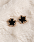 Pair of gold tone black enamel clover CZ pave stud earrings laid on cream white fluffy fur fabric showing full clover silhouette with sparkling cubic zirconia pave border and deep black enamel centre