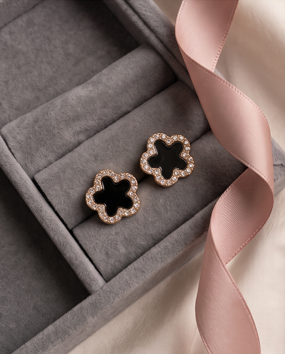 Extreme macro close up of single gold tone black enamel clover CZ pave stud earring on cream ribbed knit fabric showing individual cubic zirconia stones in pave border and glossy black enamel clover centre