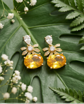 Citrine Bow & Crystal Drop Earrings - both earrings flat lay on tropical monstera leaf with white flowers