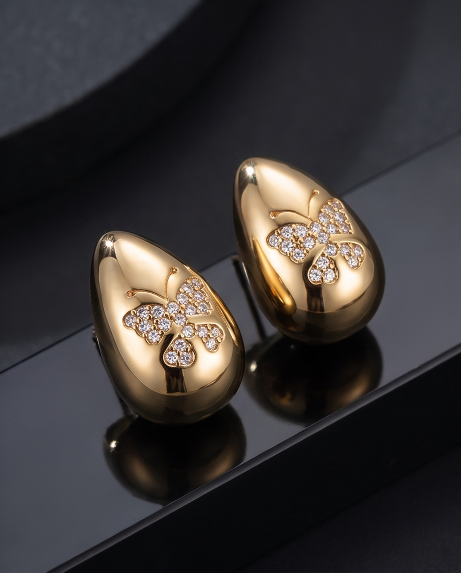 Gold Puffed Teardrop Butterfly Pavé Earrings - pair displayed on dark reflective surface with dramatic lighting