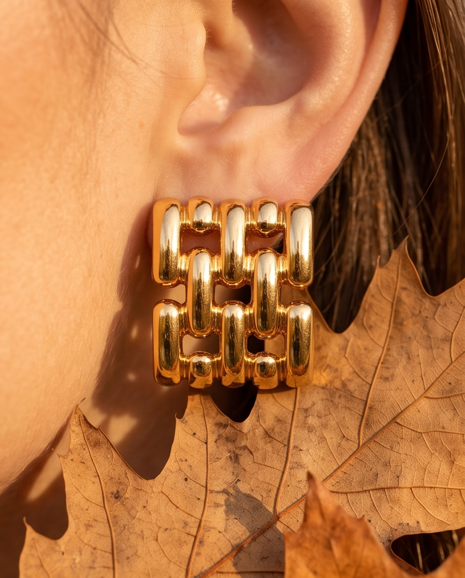 Close-up of gold chain-link square stud earring worn on ear with autumn leaf