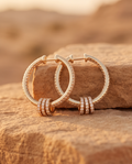 Rose gold pavé crystal knot hoop earrings resting on sandy desert rock in golden hour light