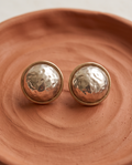 Pair of gold rim hammered silver dome button stud earrings resting on terracotta ceramic dish showing full dome and rim detail