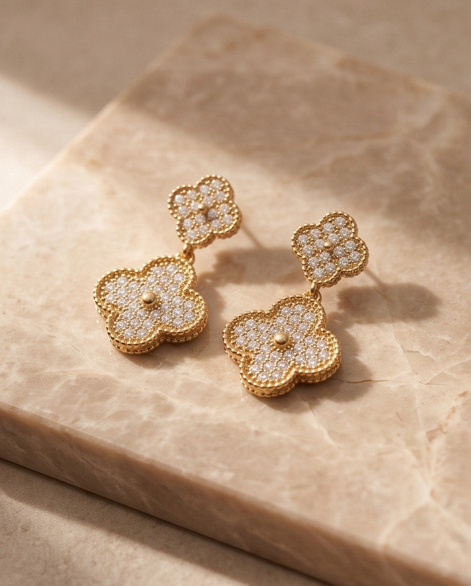 Gold pavé crystal double clover drop earrings styled on marble surface at an angle showing depth and dimension