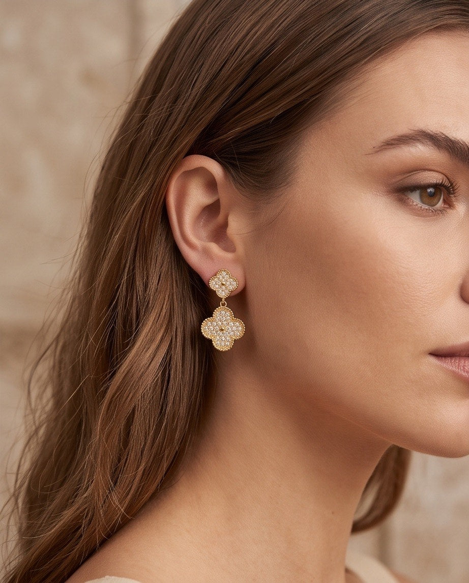 Model wearing gold pavé crystal double clover drop earrings in profile view with hair down and soft beige background