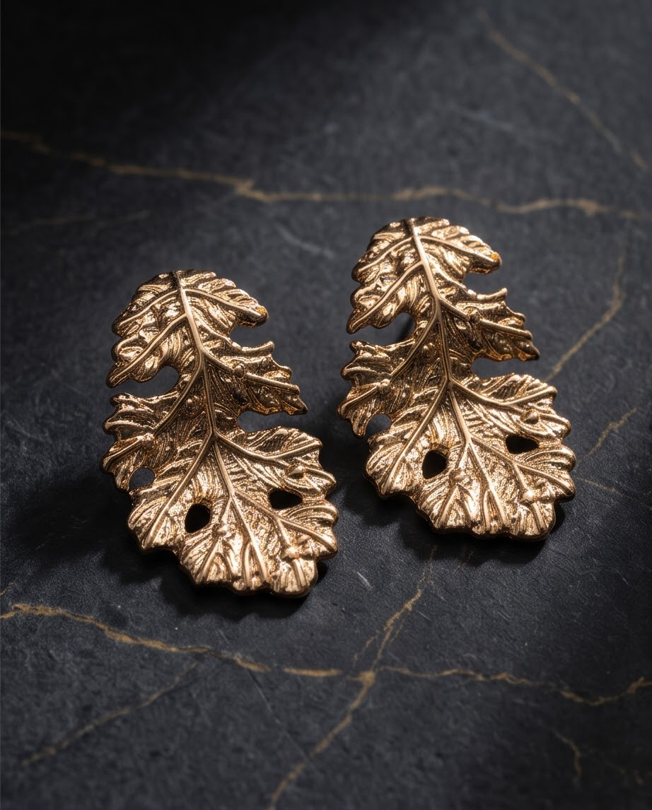 Gold botanical leaf stud earrings pair flat lay on black marble