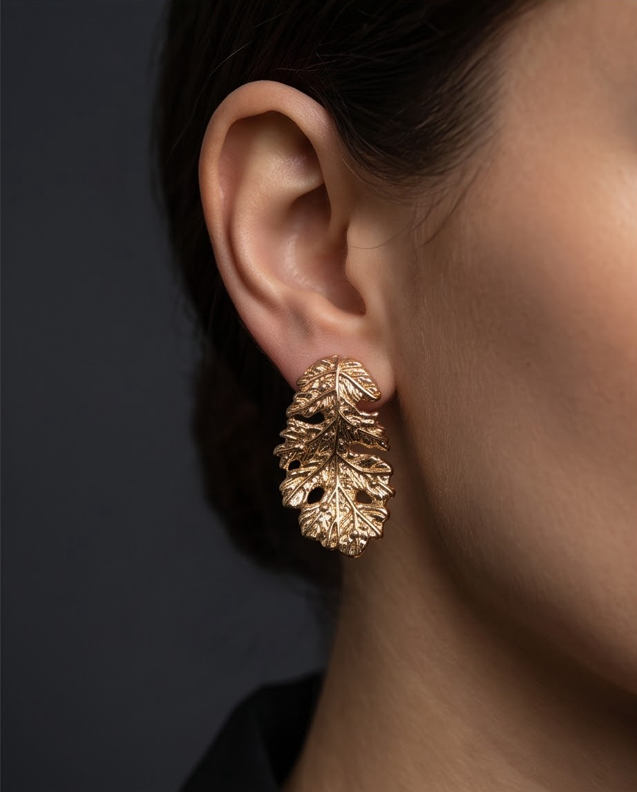 Gold botanical leaf stud earring worn on model close-up ear shot