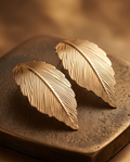 Gold Textured Feather Leaf Statement Earrings pair on stone surface