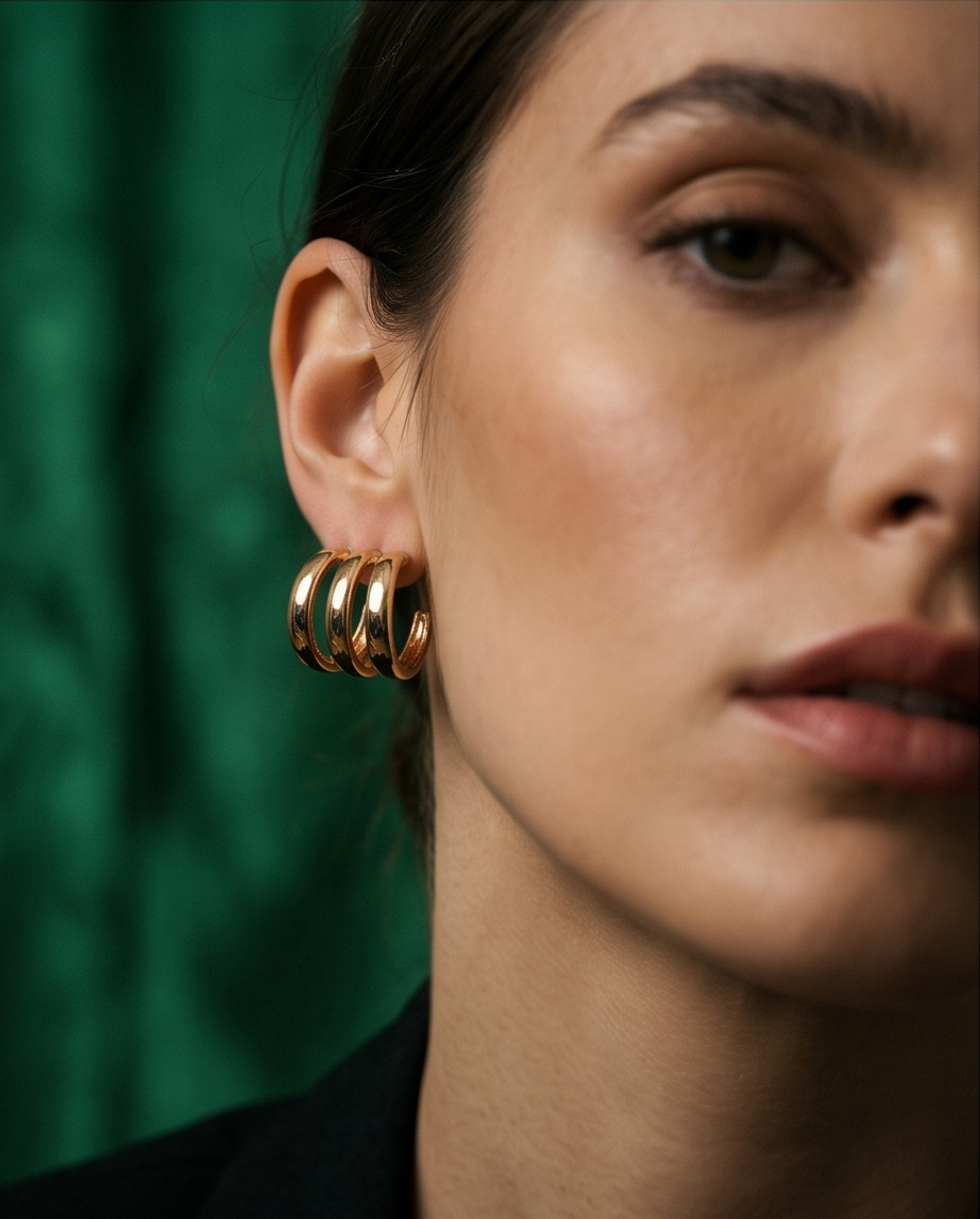 Gold triple band chunky hoop earrings worn on model against green silk backdrop