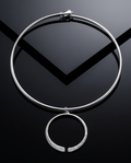 Silver torque collar with open circle pendant on dark reflective surface