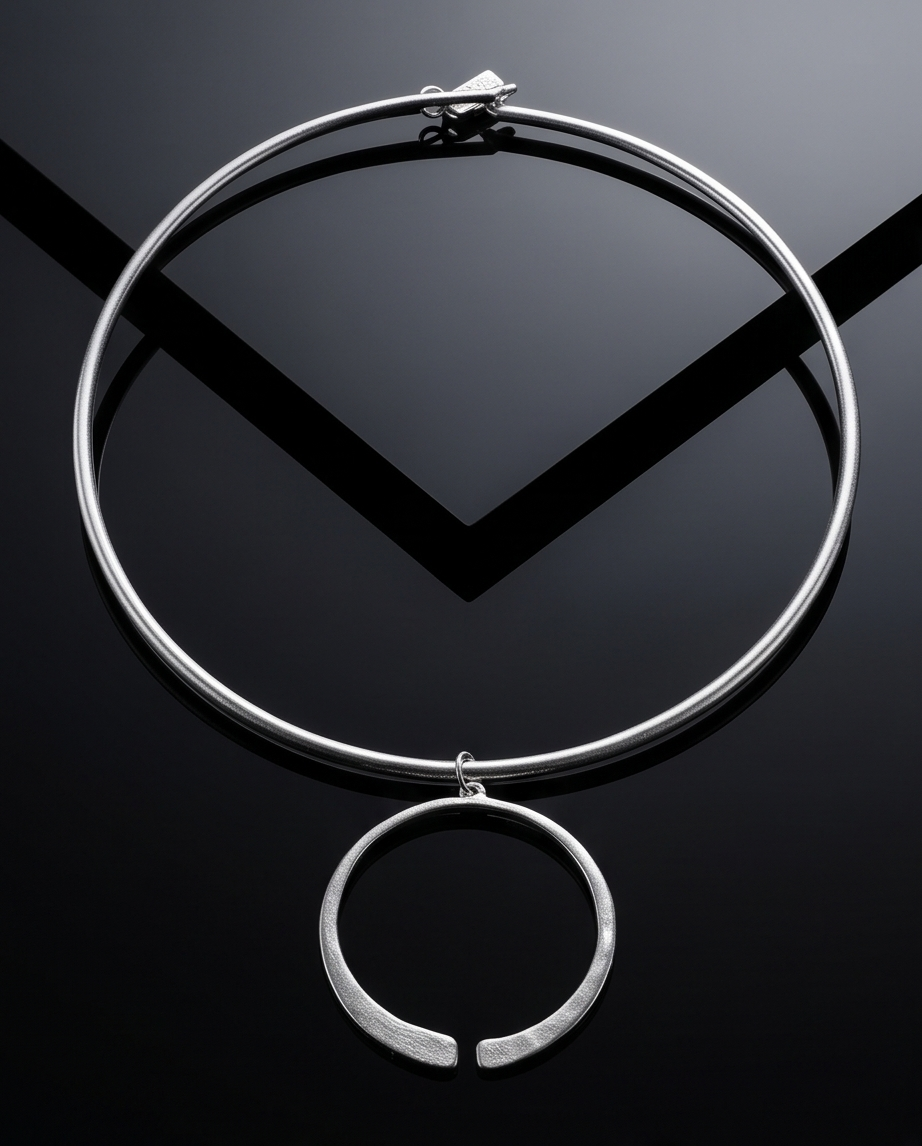 Silver torque collar with open circle pendant on dark reflective surface