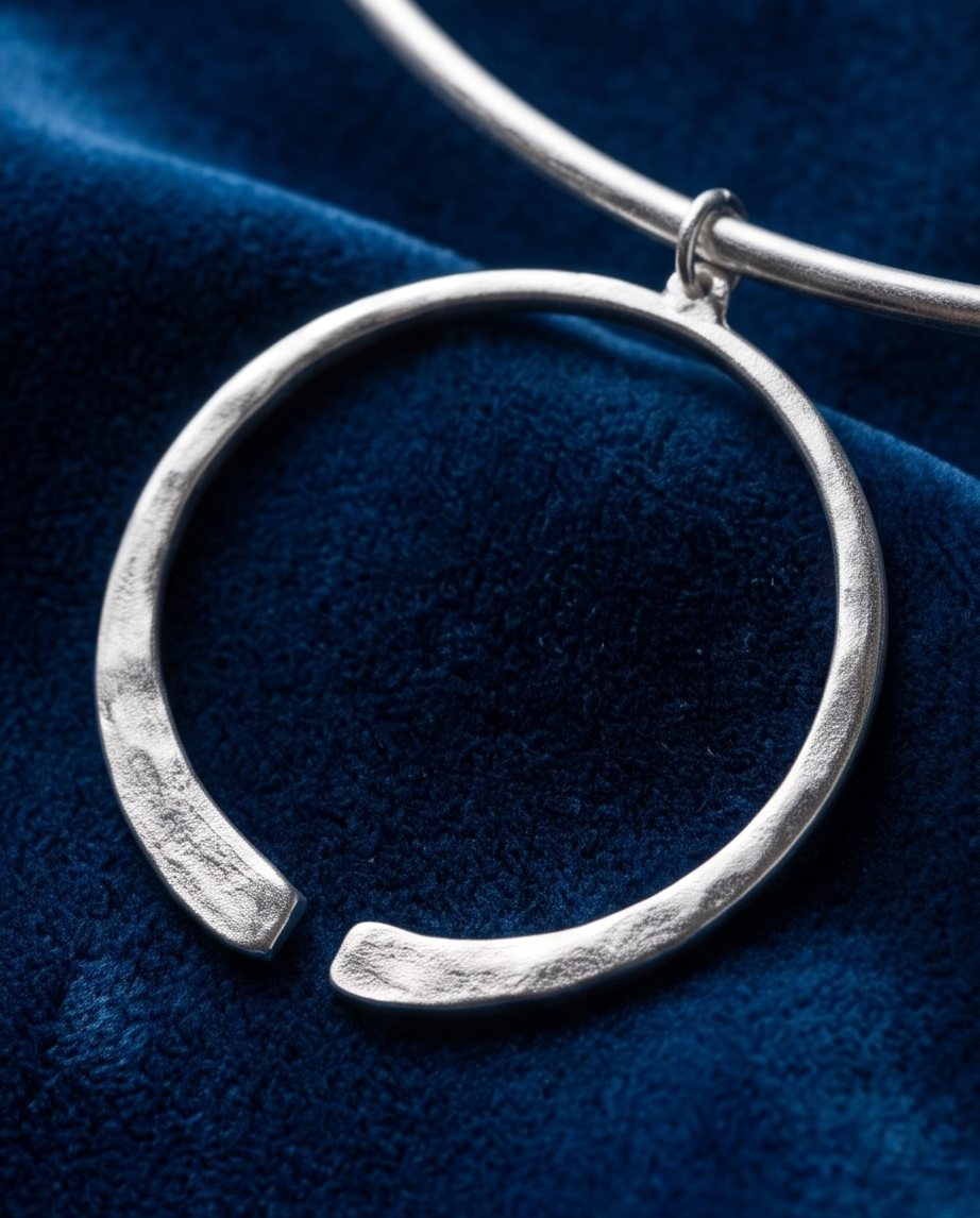 Silver torque collar with open circle pendant on black marble flat lay
