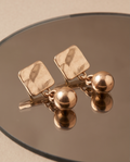 Hammered square and sphere gold-tone drop earrings on display blocks