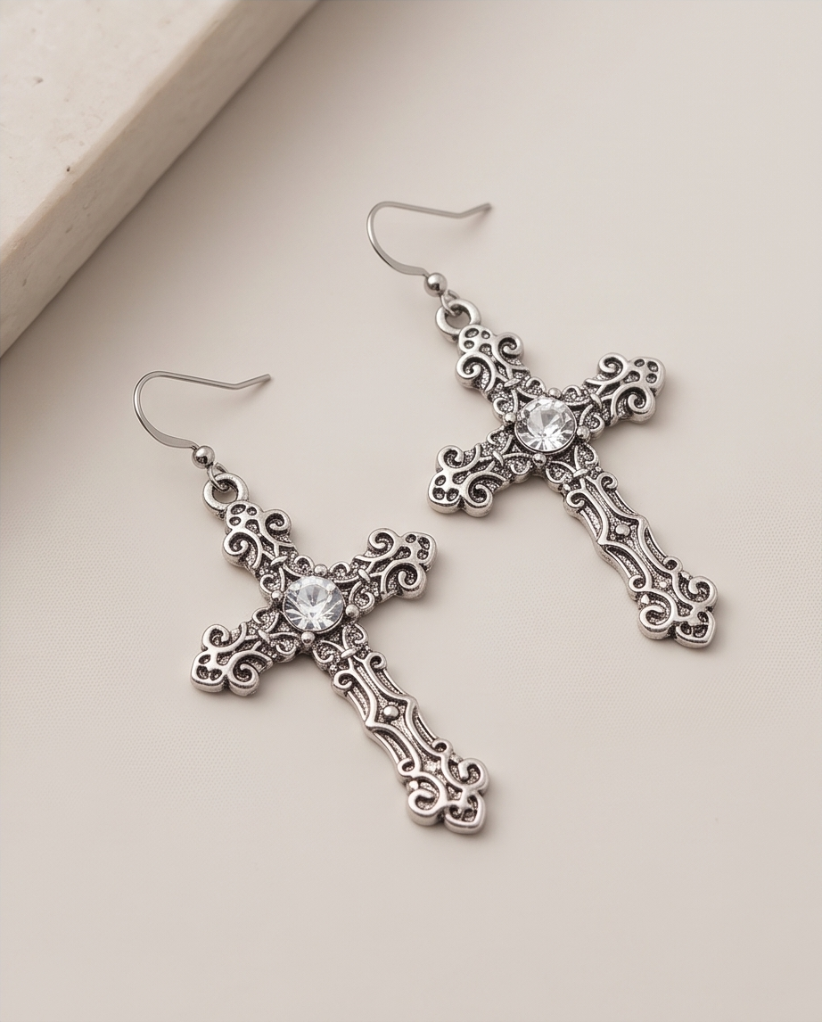 Gothic cross drop earrings styled against a pale stone edge