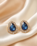 Pair of deep blue teardrop halo earrings on ivory fabric