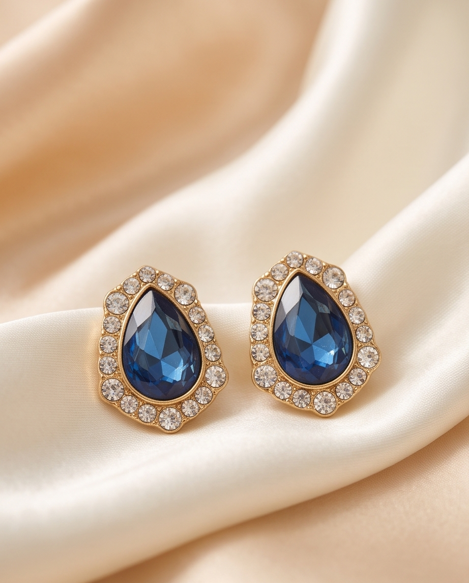 Pair of deep blue teardrop halo earrings on ivory fabric