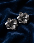 Pair of textured silver-tone flower statement earrings on navy fabric