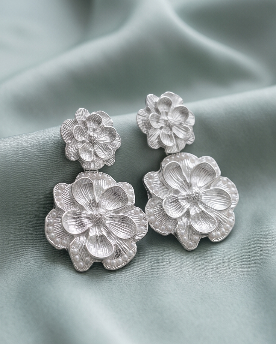 Pair of silver-tone layered floral drop earrings on pale blue fabric