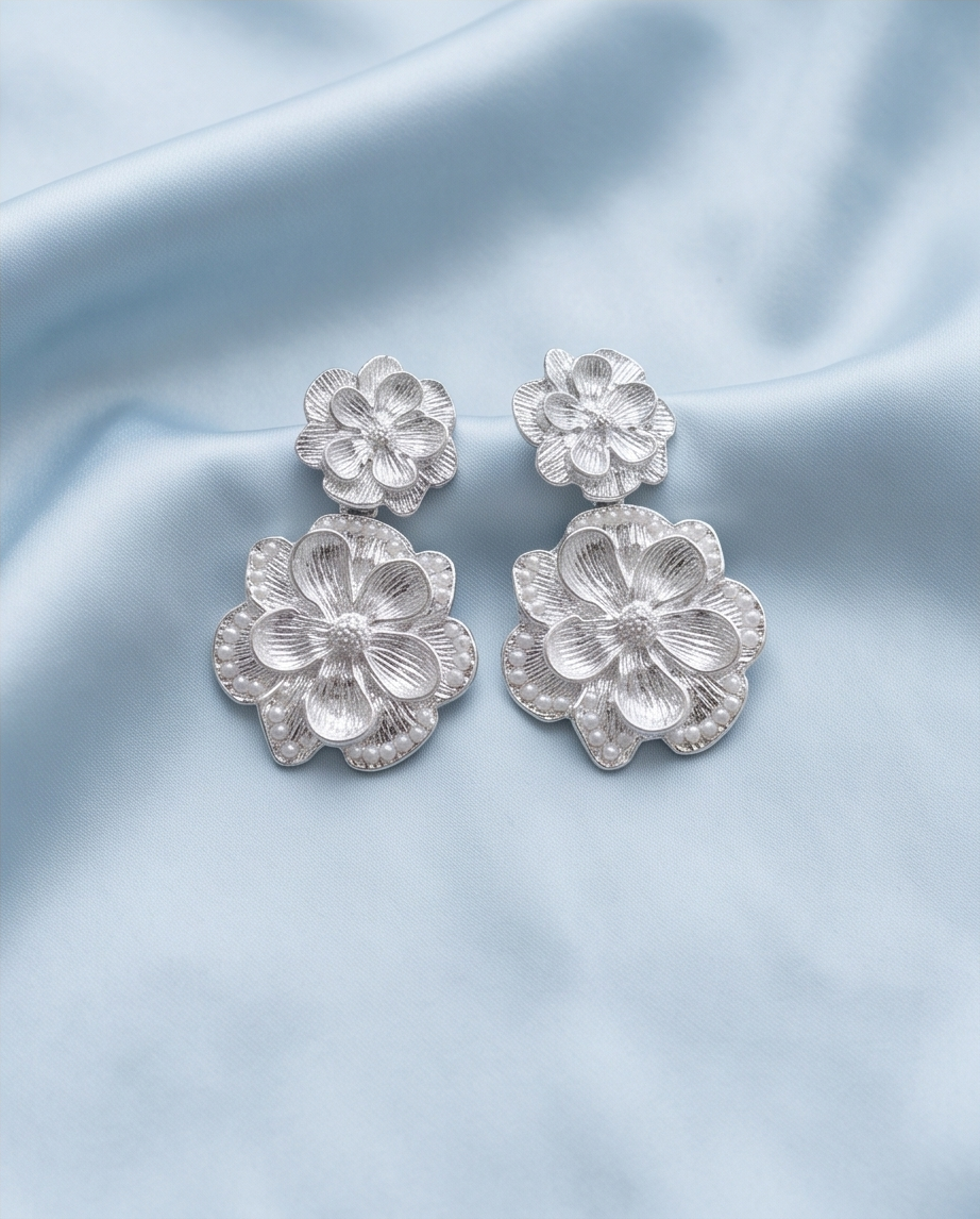 Front view of silver-tone layered flower drop earrings on blue fabric