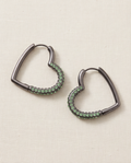 Pair of heart-shaped hoop earrings with green crystal detailing and a dark metallic finish on neutral fabric