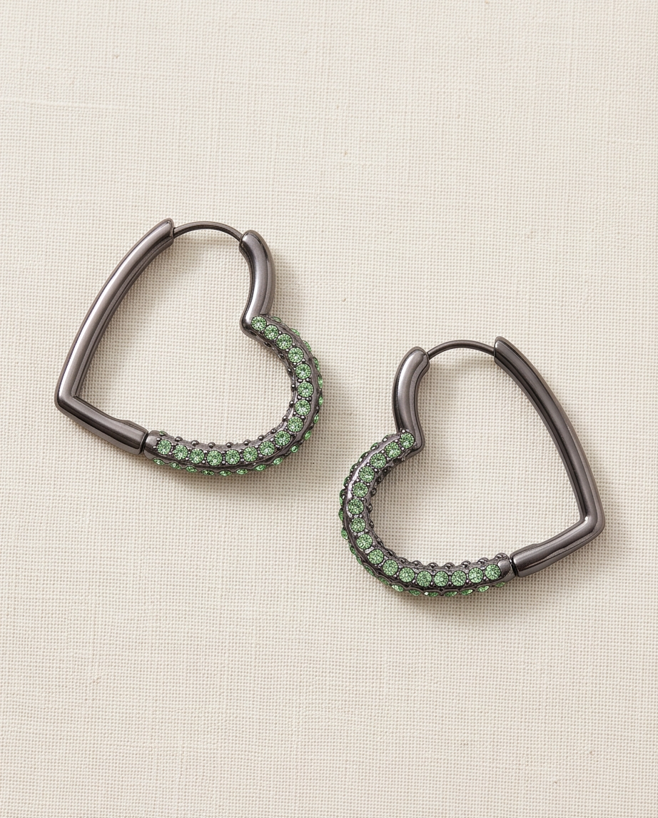 Pair of heart-shaped hoop earrings with green crystal detailing and a dark metallic finish on neutral fabric