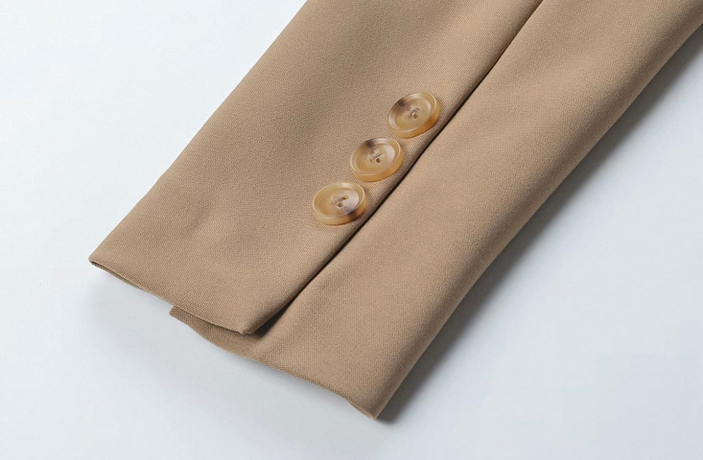 Close-up of a beige suit jacket sleeve with three round, light brown buttons, laid flat on a white background.