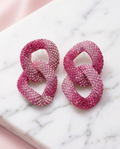 Pink crystal pavé chain link drop earrings on marble surface
