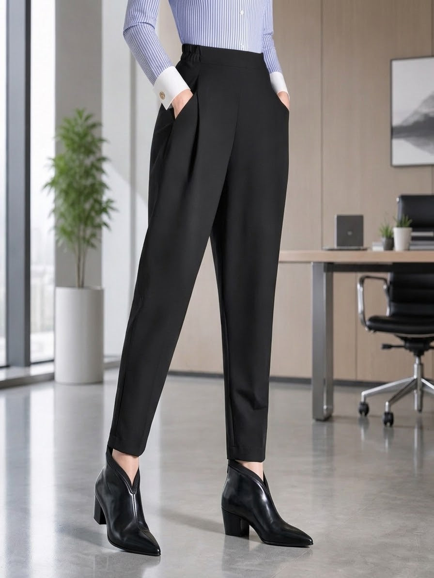 A person wearing black tailored trousers with side pockets, paired with a light blue striped long-sleeve top and black ankle boots, standing in a modern office interior.