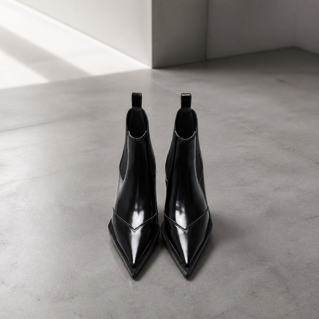 Black patent leather pointed-toe Chelsea ankle boots styled with black tote bag in luxury boutique setting