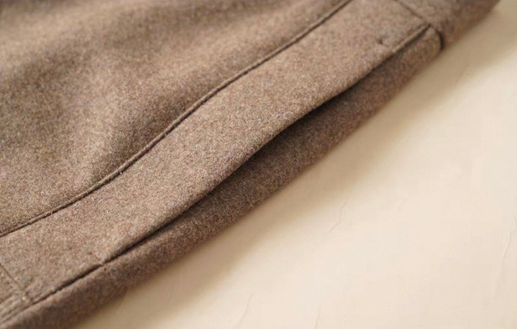 Close-up of a folded taupe wool fabric garment, showing the texture and stitching on a light cream surface.