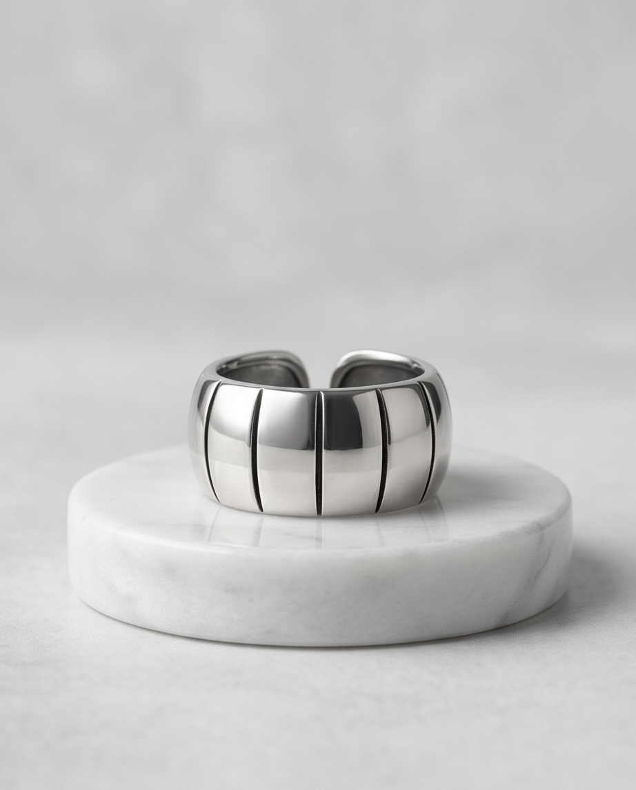 Silver chunky grooved wide band open ring on white marble pedestal against grey background