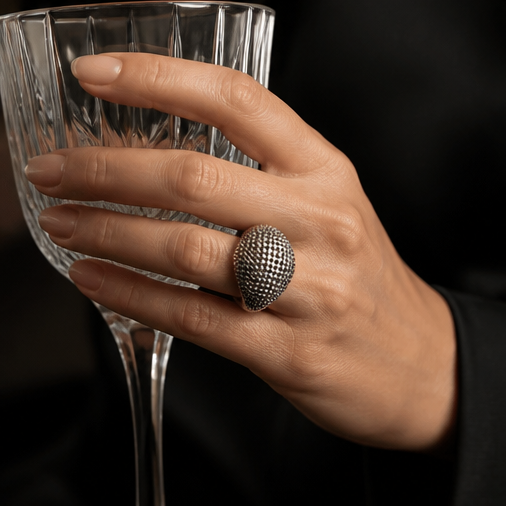 Gunmetal dome pavé ring worn on hand holding crystal glass
